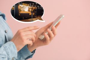 A person holding a smartphone is shown in the foreground, with a thought bubble containing an image of a well-lit food truck in the background. This image highlights the importance of modern and appealing food truck design website.