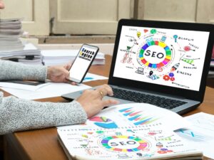 Person analysing SEO strategies on a laptop and smartphone, surrounded by charts and diagrams on a desk. Image illustrates the best podcast website design.