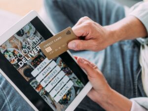 A person using a tablet and credit card to access a food delivery online ordering system for secure payments.