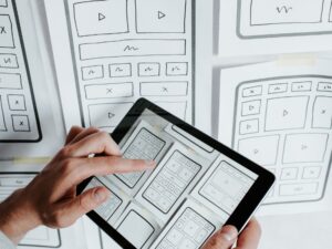 Designer reviewing wireframes for financial website designs on tablet against paper sketches