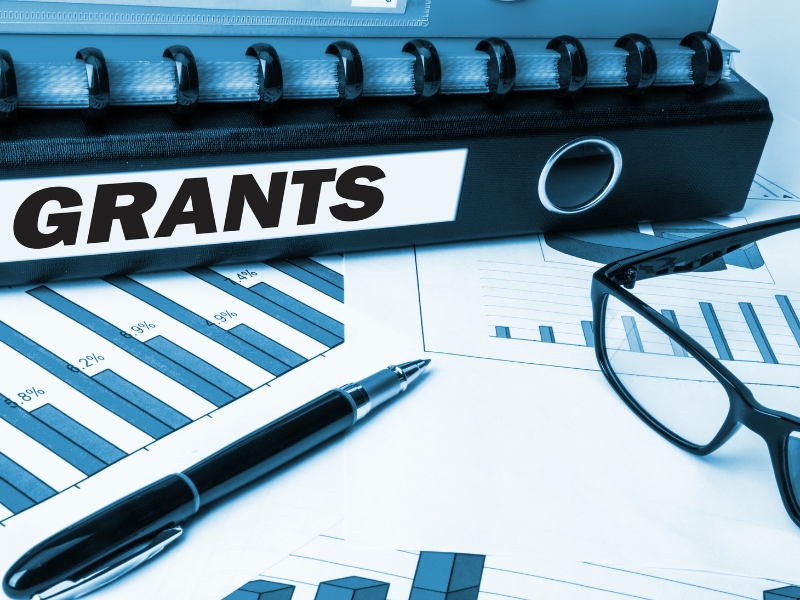 Business growth program grants binder with financial charts and glasses on desk.