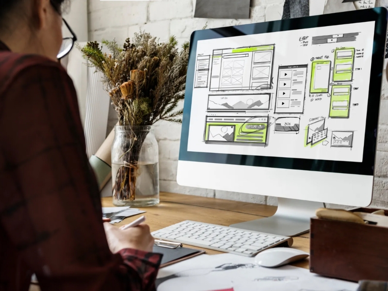 Designer creating custom web design solutions with website wireframes on computer.