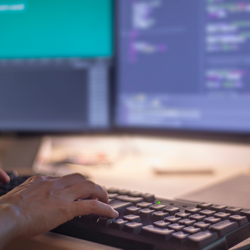 Hands typing on a keyboard in front of dual monitors showing code for professional website development.
