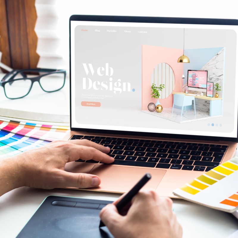 Designer using a graphics tablet beside a laptop displaying a website design agency homepage project. (